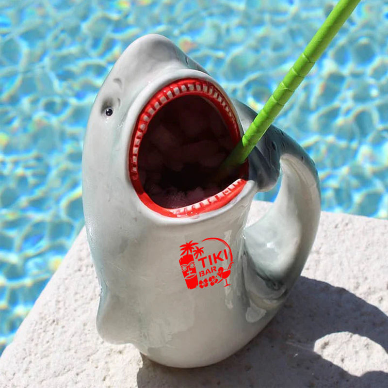 Shark-shaped mug with open mouth and red interior, featuring a 'Tiki Bar' logo, against a poolside background.
