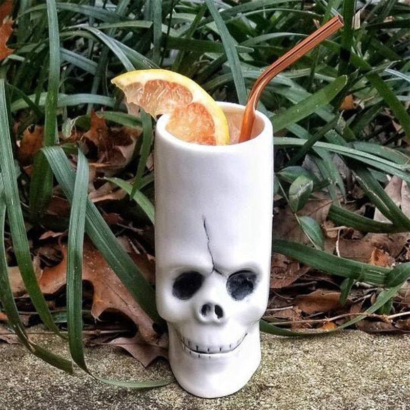 Skull-shaped glass with a drink and orange slices on a grassy background