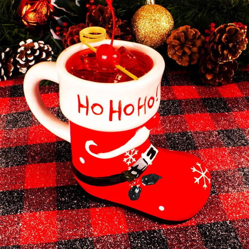 Red mug with 'Ho Ho Ho!' text, filled with a red liquid and a cherry, on a checkered background with Christmas decorations.